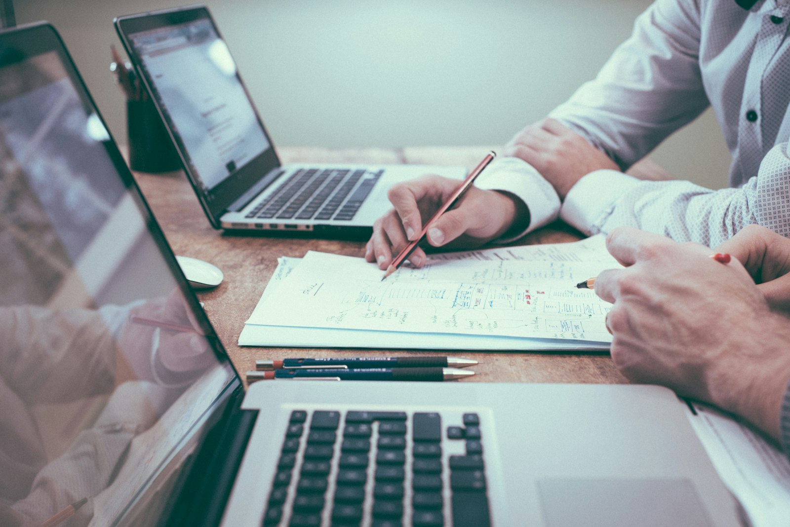 Two people reviewing printed documents together across a wooden desk.
