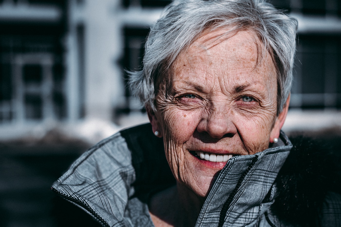 Portrait of an older woman with silver hair, smiling warmly in winter light.