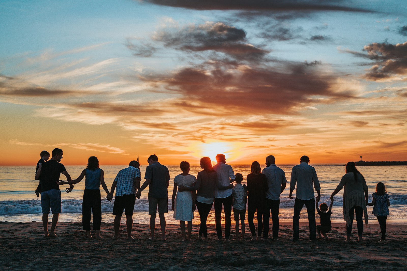 Several generations of one family standing together on a shoreline at dusk.