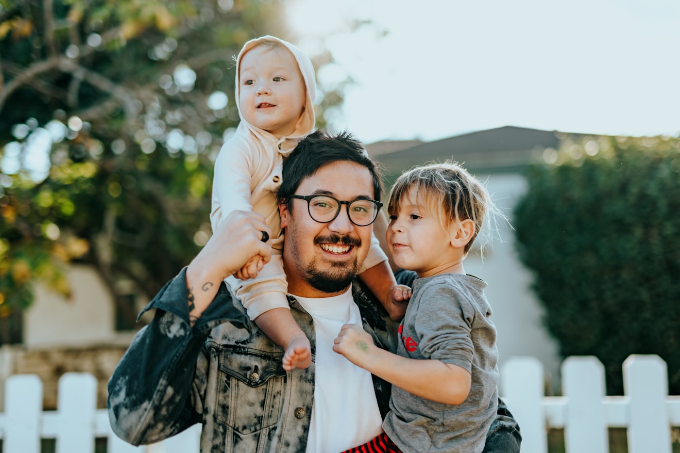 A father outdoors carrying his two young children.