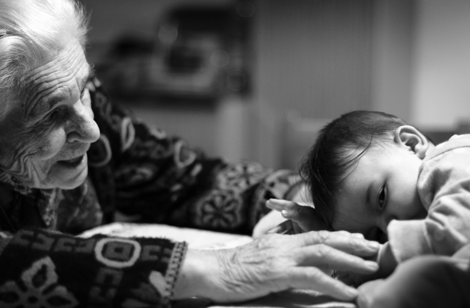 A grandmother reaching gently toward her infant great-grandchild.