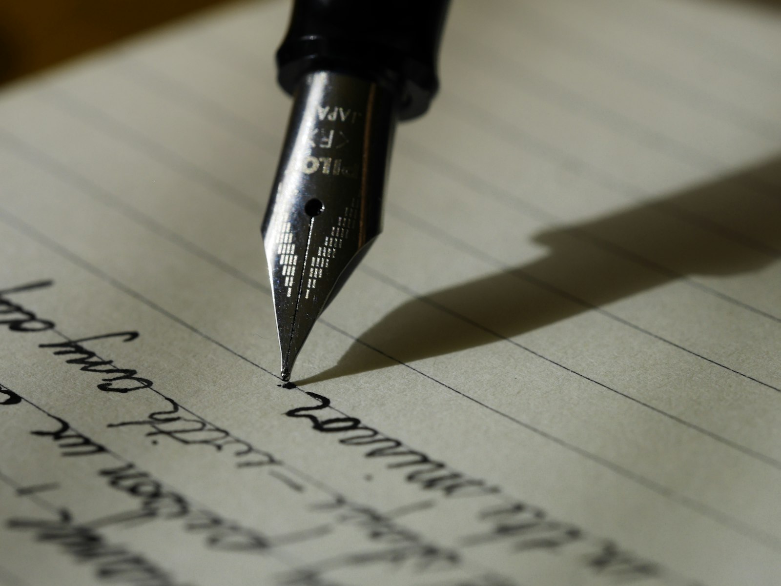 A hand holding a fountain pen, mid-sentence on a lined page.
