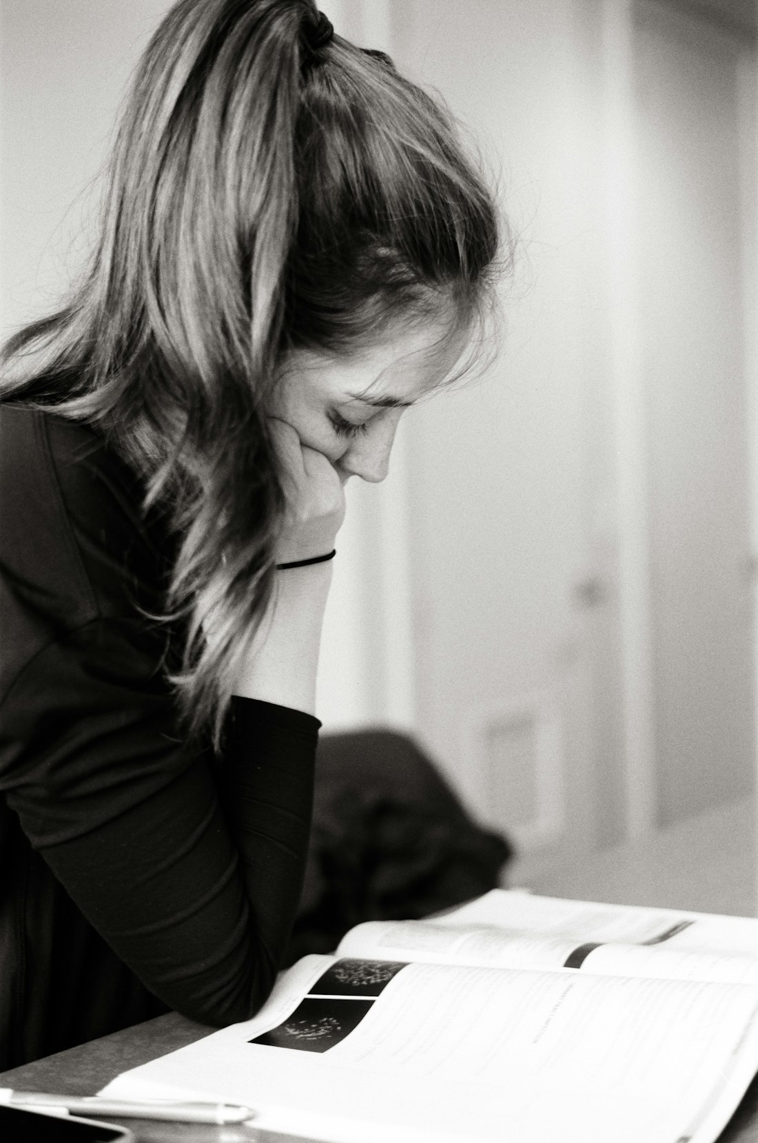 A woman reading intently, head resting on her hand, over an open reference book.
